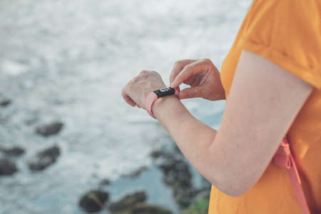 Woman hiker using smart bracelet during trekking in nature. Close up of female hands with portable...