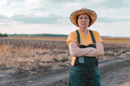 Female corn farmer looking over cornfield, portrait of woman agronomist with straw hat and jeans bib overallsの写真素材