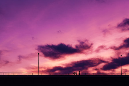 Silhouettes of three unrecognizable young people crossing the bridge in sunset with beautiful purple...