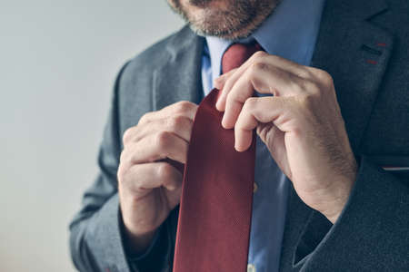 Businessman in elegant suit tying a red necktie, close up with selective focus