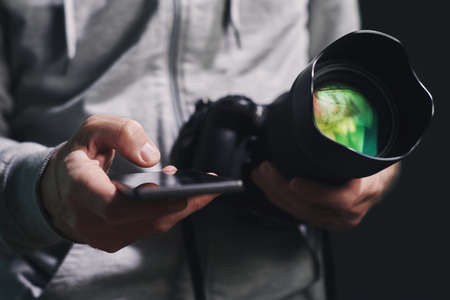 Photographer using smartphone app while holding camera in hands, selective focusの写真素材