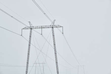 Electricity pylons and powerlines in cold foggy winter morning, abstract minimal composition with copy spaceの写真素材