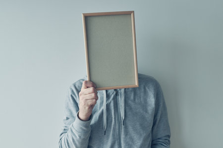Casual man holding blank picture frame in front of his face as copy space for text of graphics