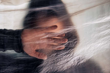 Drug addiction concept, blurred male person with hoodie behind plastic curtain, selective focus