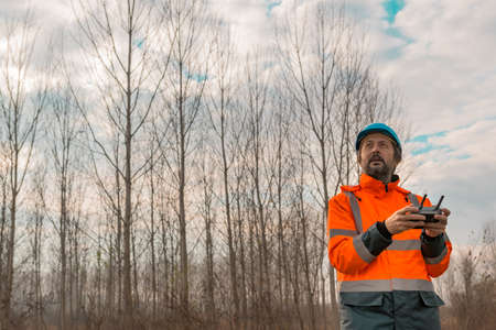 Forestry technician flying a drone with remote controller in woods and making aerial photos of forestの写真素材