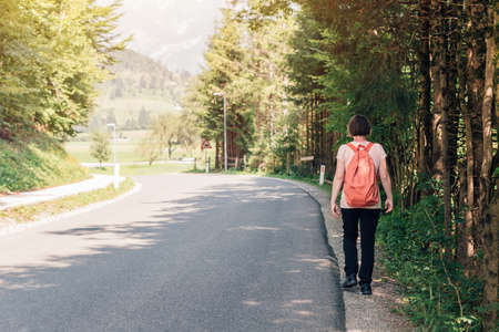 Female hiker walking by the road through countryside, rear view of woman hiking down the roadway on...