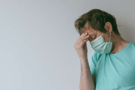 Man with mask having migraine headache as Covid-19 symptoms, portrait of male person with virus infection during pandemicsの写真素材