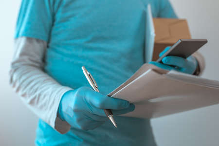 Delivery man with protective clothing using smartphone with protective gloves during viral infection...