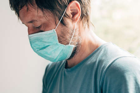 Depressed man with protective mask in self-isolation quarantine during virus outbreak pandemic,...