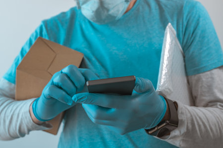Delivery man with protective clothing using smartphone with protective gloves during viral infection...
