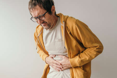 Aching stomach pain, man pressing the lower abdomen of his body with painful grimace and gastroenteritis symptoms.の写真素材