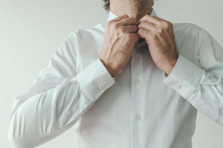 Businessman getting dressed, business person buttoning his white shirt, close up with selective focusの写真素材