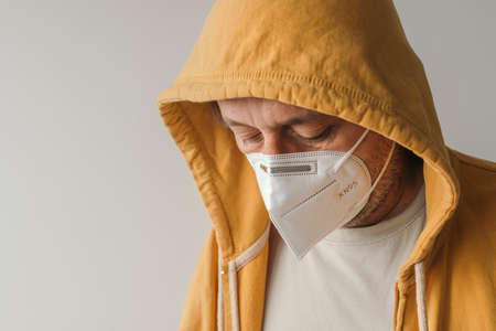 Casual male with yellow hooded jacket wearing protective respiratory KN95 face mask during covid-19 pandemics, selective focusの写真素材