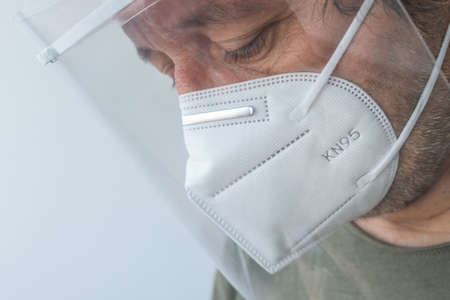 Medical professional wearing visor and KN95 respiratory mask during Covid-19 pandemics, sad and tired doctor in hospitalの写真素材