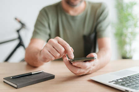 Telecommuter typing text message on mobile smart phone in home office, selective focus