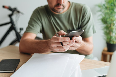 Telecommuter reading text message on mobile smart phone in home office, selective focusの写真素材