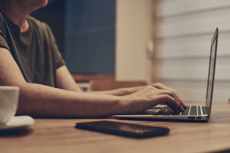 Female freelancer working from home on laptop computer in small business home office interior at night, close up of hands typing keyboardの写真素材