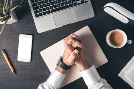 Businessman with clasped hands over work desk, top view of male business person feeling fear, anxiety or insecurityの写真素材