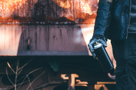 Homeless man spray painting old train wagon with aerosol can. Unrecognizable male person hand close up in conceptual image with selective focus.の写真素材