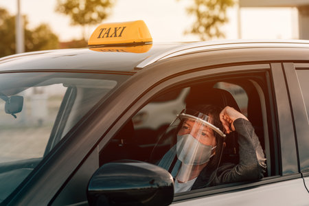 Female taxi driver with protective face mask and plastic visor waiting in carの写真素材