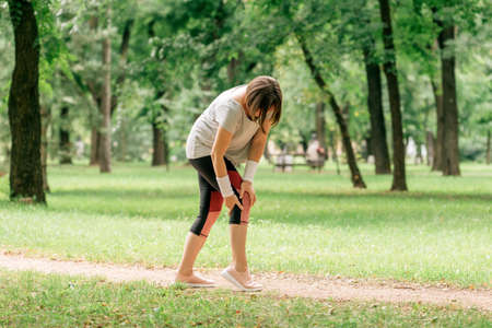 Female jogger with painful knee injury during park jogging activity, selective focusの写真素材