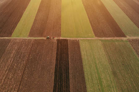 Aerial view of two farm tractors tilling in cultivated fields, drone pov high angle viewの写真素材