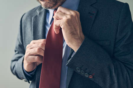 Businessman in elegant suit tying a red necktie, close up with selective focusの写真素材