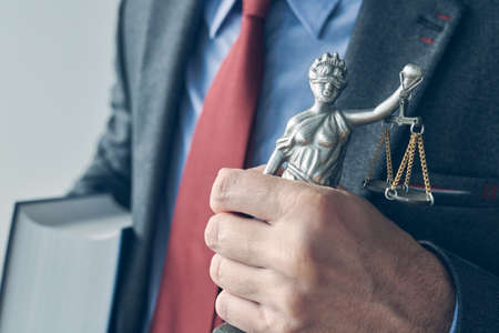 Attorney holding law book and statue of Lady Justice, close up of hand with selective focus