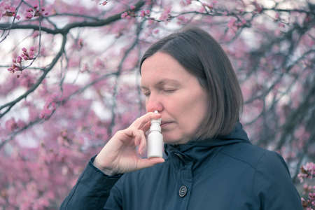 Woman using nasal spray outdoors for tree pollen allergy treatmentの写真素材