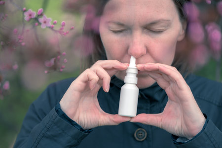 Woman using nasal spray outdoors for tree pollen allergy treatmentの写真素材