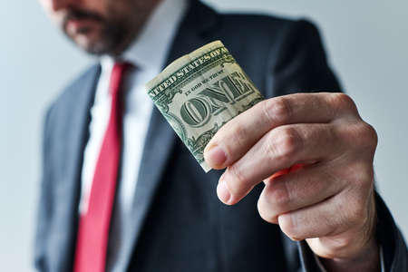 Businessman giving one dollar tip, close up of hand selective focus of a male businessperson holding american paper currency banknoteの写真素材