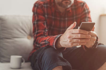 Taking a break on mobile smart phone while working from home, man using phone at living room sofa, selective focusの写真素材