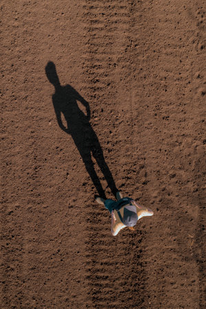 Female farmer standing in ploughed field casting long shadow on the ground, copy space included