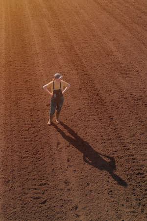 Female farmer looking over ploughed field, drone photography high angle view, copy space includedの写真素材