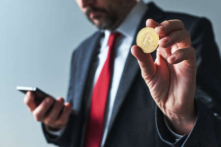 Businessman using mobile smart phone app for Bitcoin mining, close up with selective focus