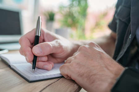 Freelancer writing notes in a notebook while working in home office, selective focus