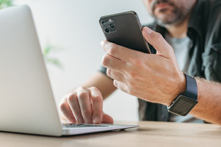 Freelancer using laptop computer and mobile smart phone at the same time, multitasking concept with...