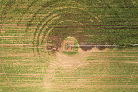 Aerial view of center pivot irrigation equipment watering green soybean seedlings on farm plantation, drone pov footageの写真素材