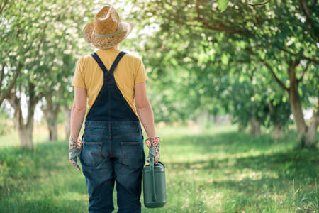 Female farmer with watering can in organic orchard, locally grown food production concept, selective...