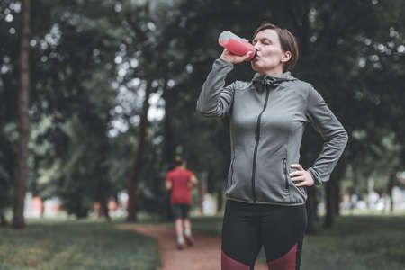 Female jogger drinking of refreshing strawberry juice in park, healthy lifestyle and recreational activity in 40sの写真素材