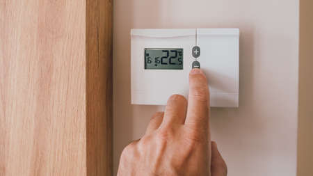 Male hand pushing the button of home heating and cooling system control unit, closeup with selective focusの写真素材