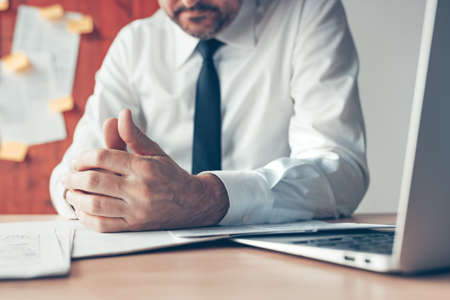 Bored businessman playing with thumbs of his hands in the office, close up with selective focus