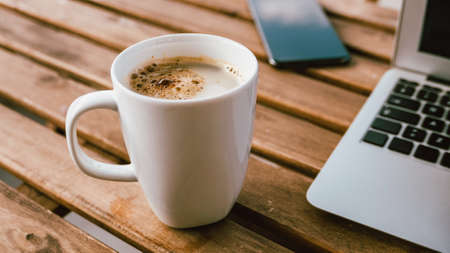 Coffee cup with laptop computer and mobile smart phone on freelancer's desk, selective focusの写真素材