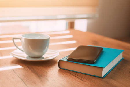 Cup of coffee, mobile smart phone and a book on the table in morning, selective focusの写真素材
