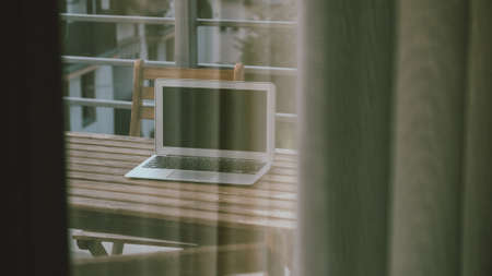 Laptop computer shut down on hotel room balcony seen through room window, working on vacation concept, selective focusの写真素材