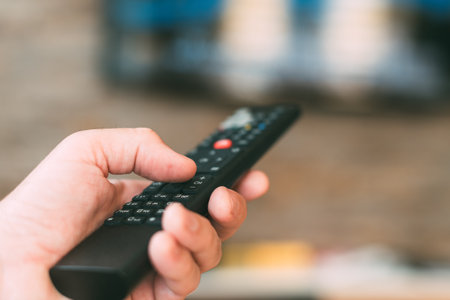 Male hand holding television remote controller, close up with selective focusの写真素材