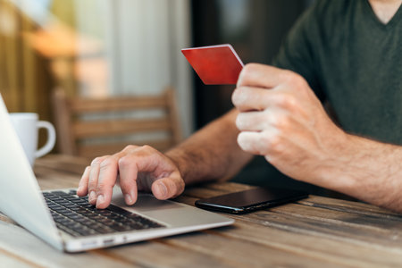 Online shopping from home balcony, man using laptop computer, mobile smart phone and credit card to purchase items on internet, selective focusの写真素材