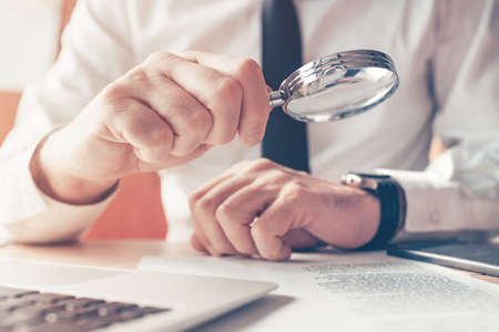 Cautious businessman reading contract agreement with magnifying glass, close up with selective focusの写真素材