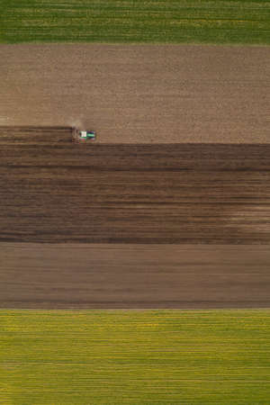 Aerial view of agricultural tractor tilling and harrowing ploughed field, directly above drone pov...