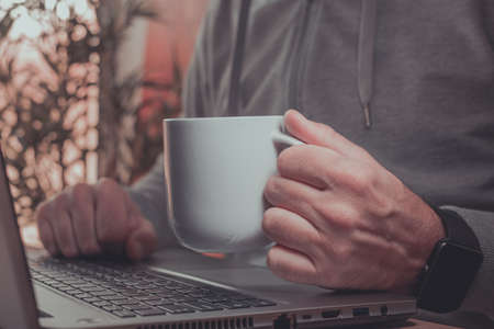 Freelancer is drinking coffee and working from home on laptop computer, selective focus